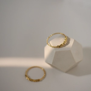 Vue détaillée de deux bagues minimalistes dorées avec perles sous des ombres de lumière naturelle