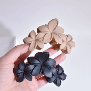Matte beige and black triple flower hair claws held in hand on white background