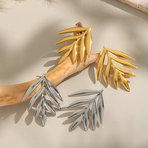 Minimalist leaf-shaped stainless steel stud earrings in gold and silver on wood branches