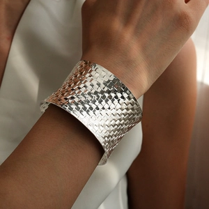 Close-up of a wide silver woven texture bangle on a wrist with reflective metallic finish