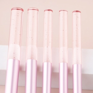 Close-up of makeup brush handles with pink glitter liquid inside clear crystal tubes