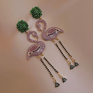 Dettaglio di orecchini a fenicottero con strass, perla verde e catene con frange nere