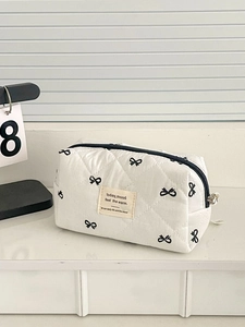 Detail of white quilted makeup bag featuring black bow patterns and zipper closure