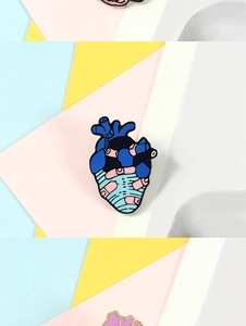 Close-up of heart-shaped enamel pin with blue and pink anatomical design on colorful background