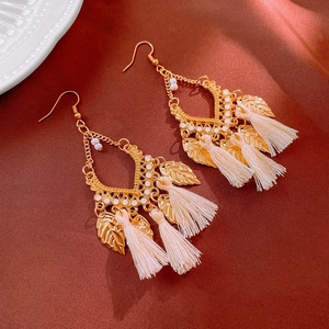 Macro shot of bohemian gold leaf earrings with cream tassels on red satin background