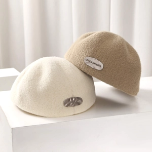 Winter beret hats in beige and camel with metal logo label on white pedestal
