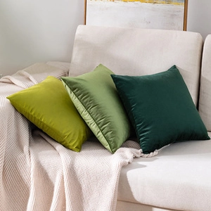 Detailed view of three green plush velvet square pillows on a cozy beige knitted blanket