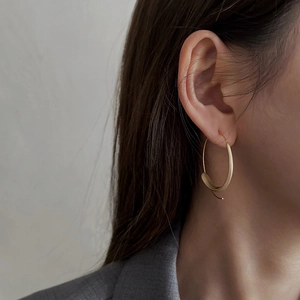 Close-up of matte gold irregular hoop earrings worn by a model in gray blazer