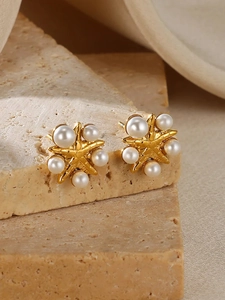 Macro detail of gold star earrings with inlaid white pearls on natural stone