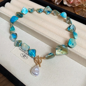 Detailed shot of irregular blue shell beads and white pearl pendant with golden OT clasp