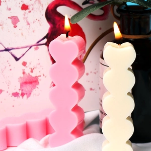 Dettaglio macro di candele a cuore impilate rosa e beige con fiamma accesa calda
