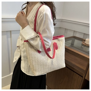 Detail of woven straw tote bag featuring bright pink faux leather shoulder straps