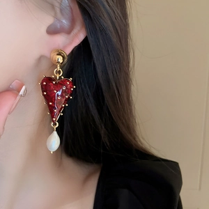 Détail de boucles d'oreilles cœur rouge texturé, touches dorées et perle baroque sur modèle