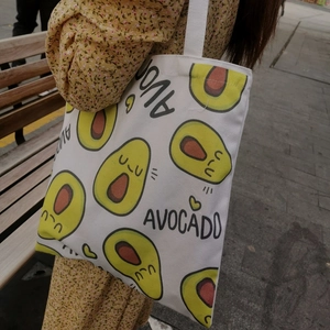 Detail van een witte canvas draagtas met avocado-opdruk vastgehouden door een persoon