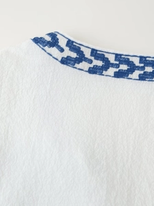 Detail of blue geometric embroidery on white cotton neckline of a vintage style blouse