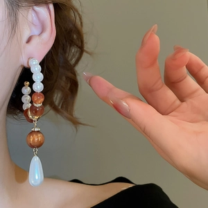 Detailed view of elegant pearl drop earrings with amber beads on a female model