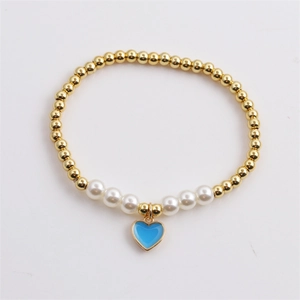 Close-up of golden beaded bracelet with white pearls and a sky blue heart pendant