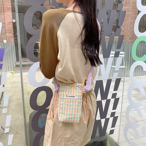 Detail of colorful plaid drawstring crossbody bag with purple padded strap and brand label