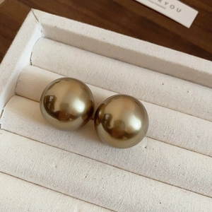 Détails de grandes boucles d'oreilles boules dorées sur un présentoir à bijoux texturé