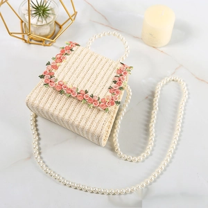 Cute mini straw woven flower bag with pearl handle and rose embroidery on marble surface