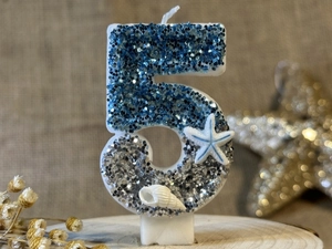Detail of ocean-themed glitter number 5 birthday candle with starfish and seashell decor