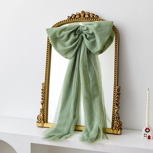 Large Morandi green organza Christmas bow hanging on a vintage gold relief mirror