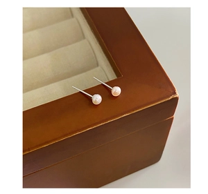 Close-up of small white freshwater pearl stud earrings on a wooden jewelry box edge