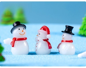 Close-up of three miniature resin snowmen with red scarves on a blue textured surface