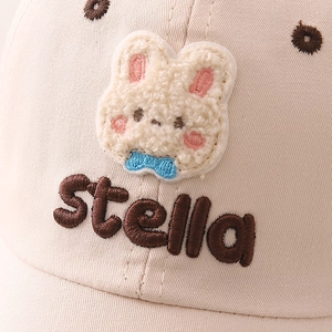 Detail of cream kids baseball cap showing plush rabbit patch and Stella embroidery
