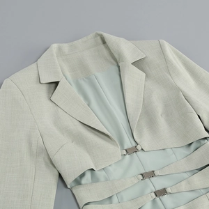 Détail d'un blazer court vert sauge avec découpes à la taille et boucles métalliques
