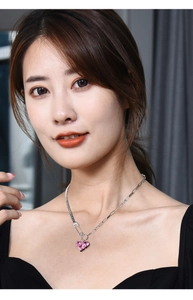 Close-up of a silver necklace with a pink heart pendant and pin clasp on a model