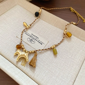 Detailed shot of golden rocking horse pendant with tassels on a woven cord necklace