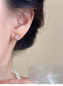 Close-up of pink square diamond stud earrings worn on ear with sparkling accents