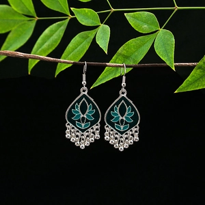 Close-up of vintage silver earrings with green enamel lotus and tassel on wooden branch