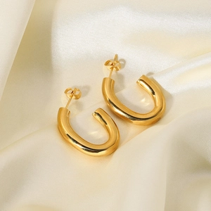 Gros plan de boucles d'oreilles ovales dorées en U sur un fond en soie champagne