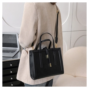 Detail of black rectangular tote bag with parallel stitching and golden metal hardware