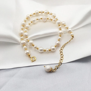 Detailed view of Baroque freshwater pearls and gold-plated beads necklace on silk fabric
