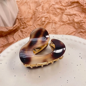 Irregular amber acetate hair claw clip with gold metal base on ceramic plate