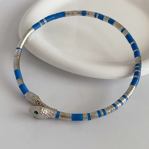 Top view of snake bracelet with silver head, blue rings, and green gemstone eyes on ceramic