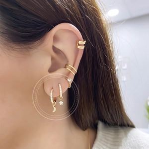 Close-up of gold star and moon drop earrings set with a minimalist double-line ear cuff