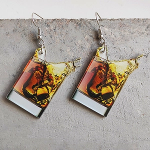 Acrylic whiskey glass earrings with ice and liquid splash on concrete surface