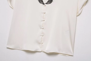 Detail der cremefarbenen Satinbluse mit schwarzem Spitzenkragen und Stoffknöpfen