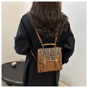 Detail of leopard print backpack showing vintage dual metal buckles and brown leather trim