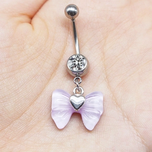 Close-up of heart navel ring with purple bow and zircon held in hand for scale