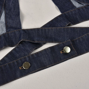 Close-up of dark blue denim strap with golden buttons and orange contrast stitching