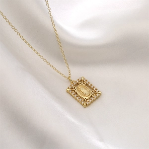 Macro detail of gold plated Virgin Mary pendant with cubic zirconia on white satin