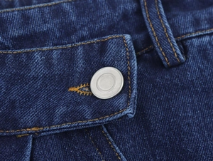 Détail du bouton métallique et des surpiqûres jaunes sur la taille du jean bleu foncé