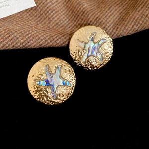Dettaglio macro di orecchini a perno martellati in oro con stella marina in abalone cangiante