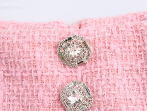 Detailaufnahme von funkelnden Strassknöpfen auf rosa Tweed-Stoff mit Fransenstruktur
