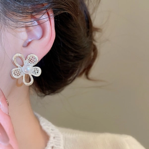 Detail shot of hollow flower earrings with white pearl center on elegant female ear